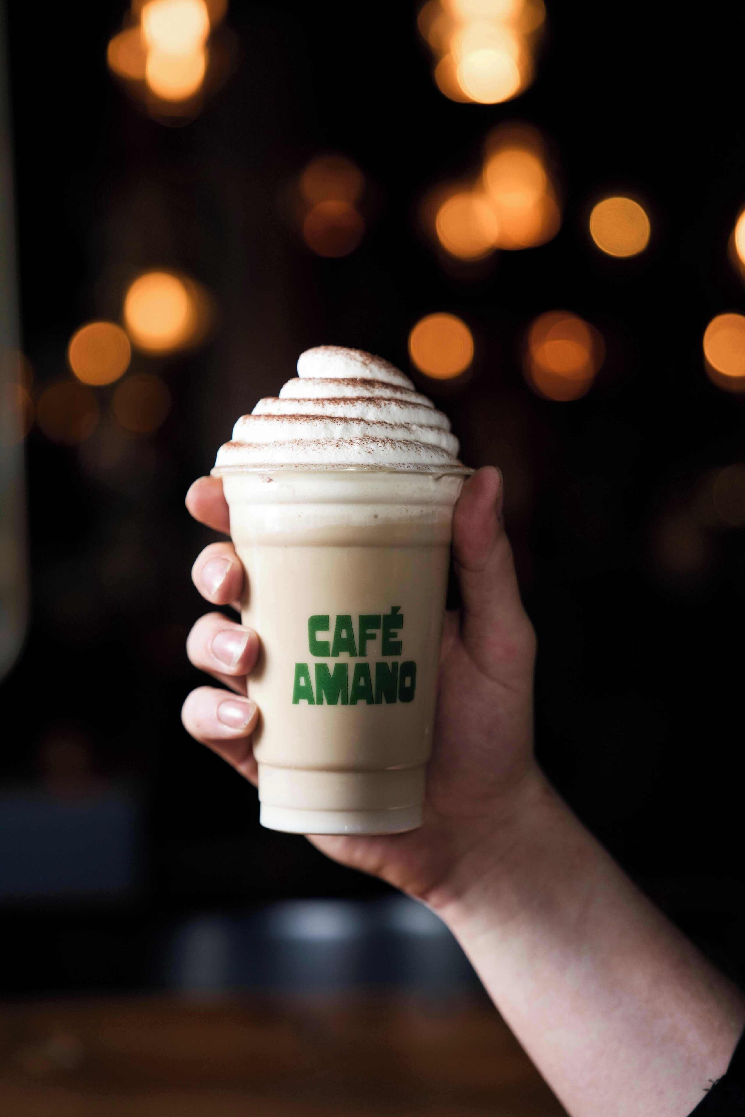 Una mano sosteniendo una taza con el texto 'CAFE AMANO'.