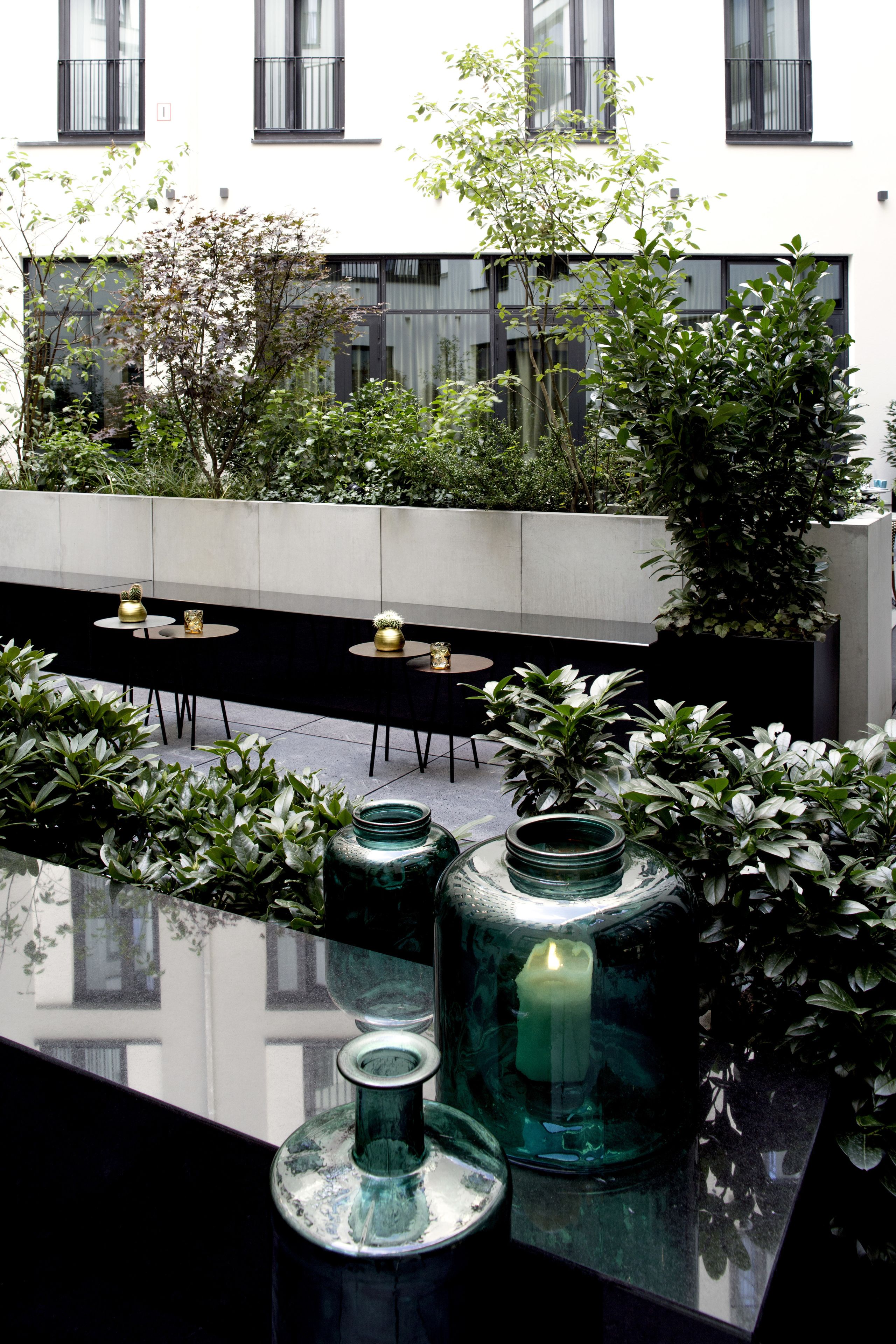 A modern outdoor seating area with tables and chairs, surrounded by greenery and decorative glass vases.