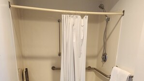 A shower area with a white curtain, grab bars, a towel rack, and a tiled floor. - Nittany Budget Motel (State College)