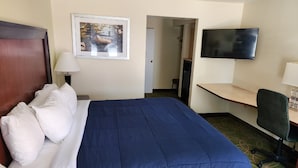 A hotel room with a bed, a desk, a chair, a TV, and a framed picture on the wall. - Nittany Budget Motel (State College)