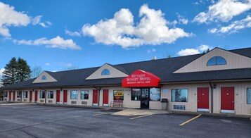 A motel with a red sign, multiple rooms, and a parking lot.