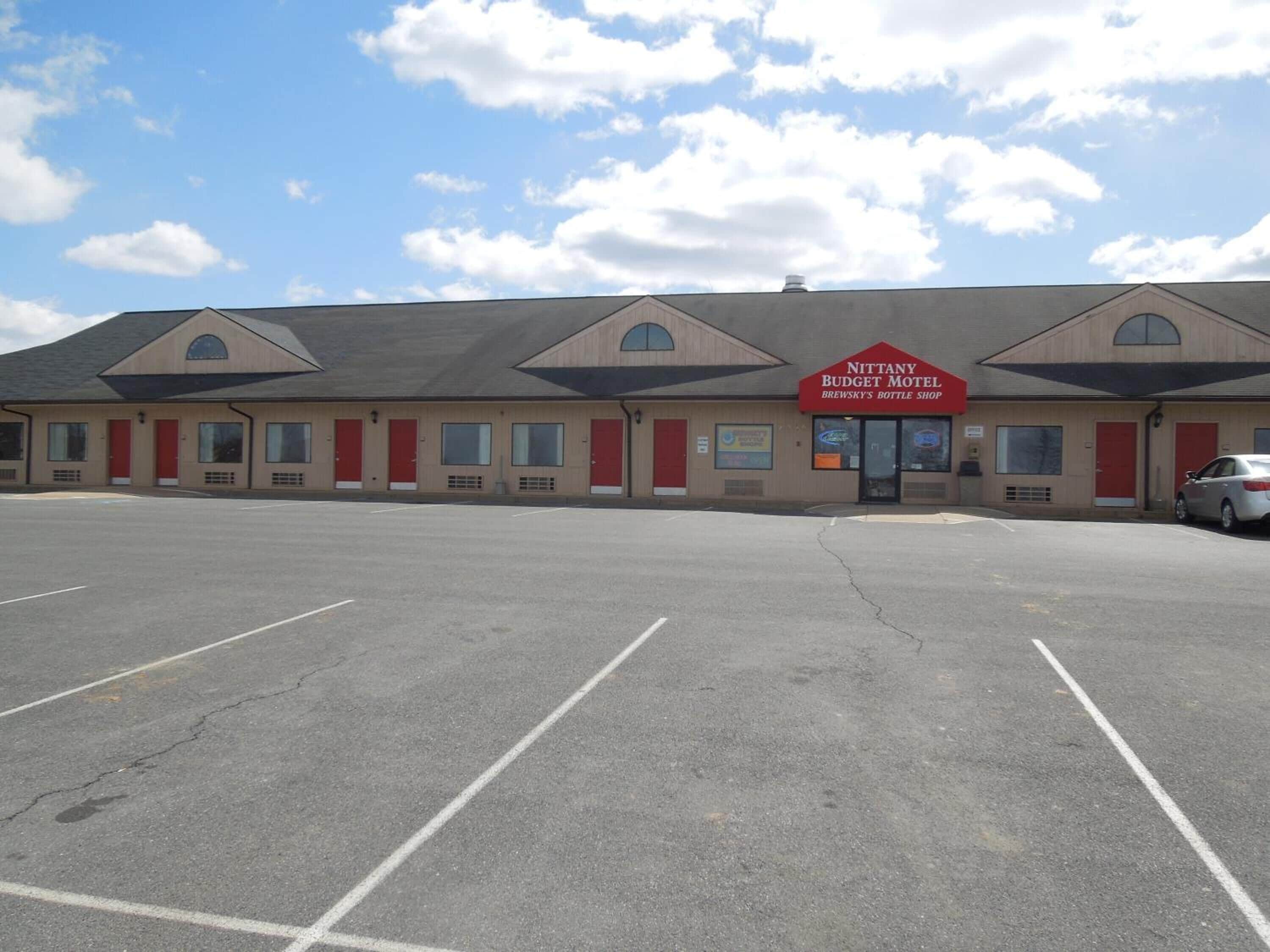 A motel with a large parking lot and a sign for Nittany Budget Motel and Brewsky's Bottle Shop.