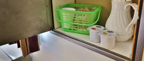 A small kitchenette with a green basket, a white pitcher, and two containers of yogurt.