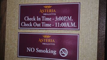 Two signs for Asteria Inn & Suites: one indicates check-in at 3:00 P.M. and check-out at 11:00 A.M., and the other states no smoking is allowed.