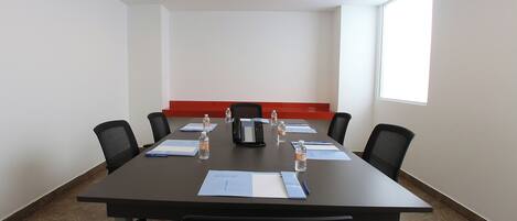 Una sala de conferencias con una larga mesa, sillas, un teléfono y documentos.