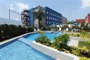 A swimming pool with a tiled edge, surrounded by greenery and white lounge chairs. - One Cuernavaca (Cuernavaca)