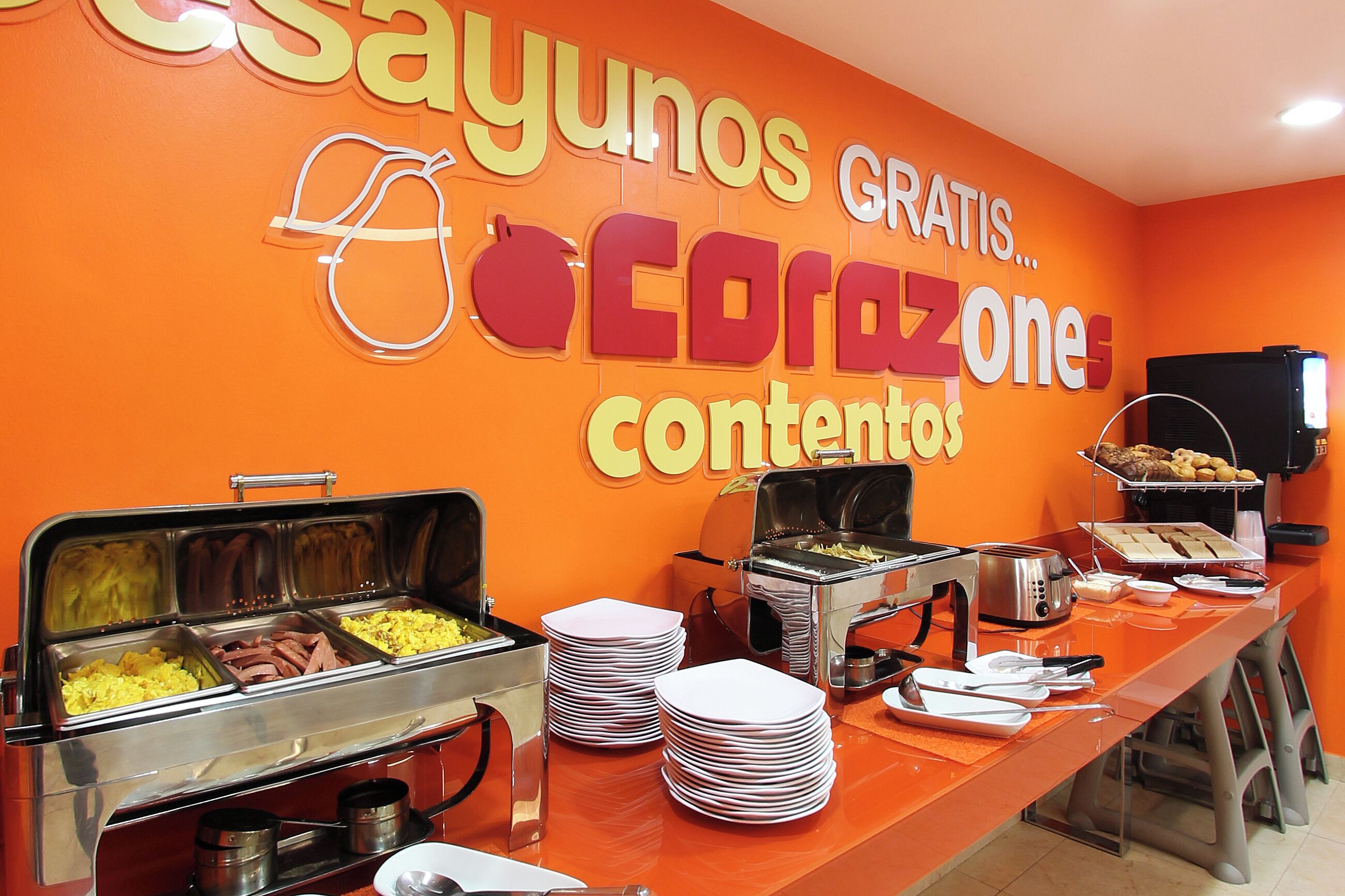 Zona de bufé con diversas opciones de comida y un letrero que dice "Sayunos Gratis... Corazon contentos".