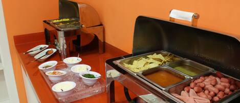 A buffet with various food items including hot dogs, nachos, and different dips.