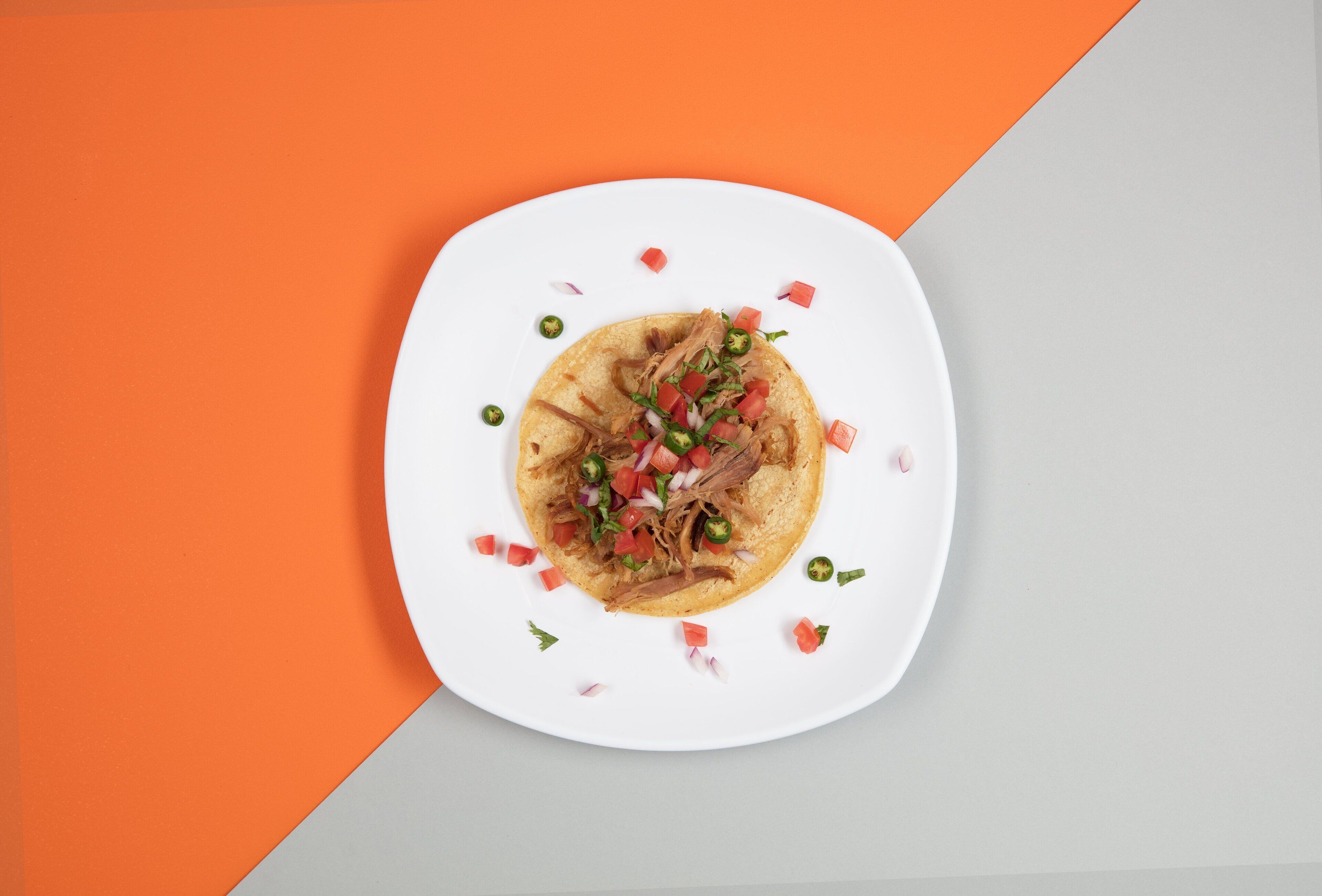 Un plato con un taco sobre una base blanca, rodeado de un fondo geométrico.