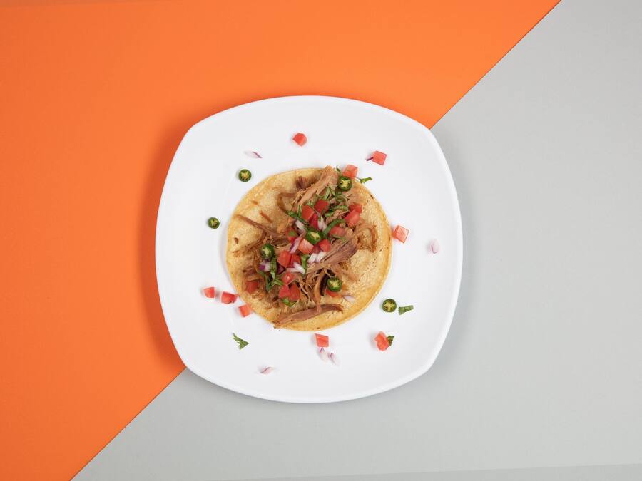 Un plato con un taco sobre una base blanca, rodeado de un fondo geométrico.