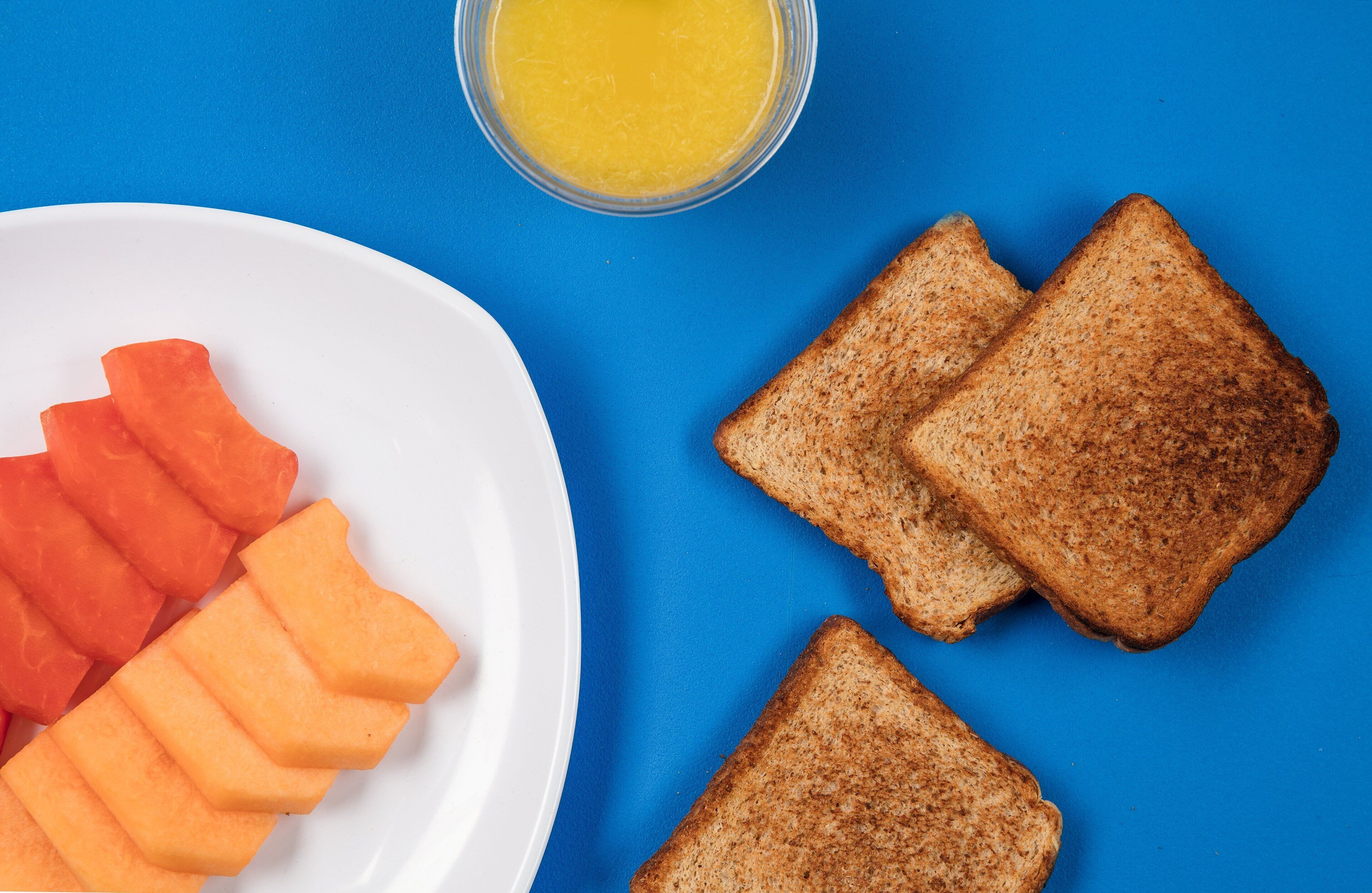 A plate with slices of toast and carrot sticks on a blue background.