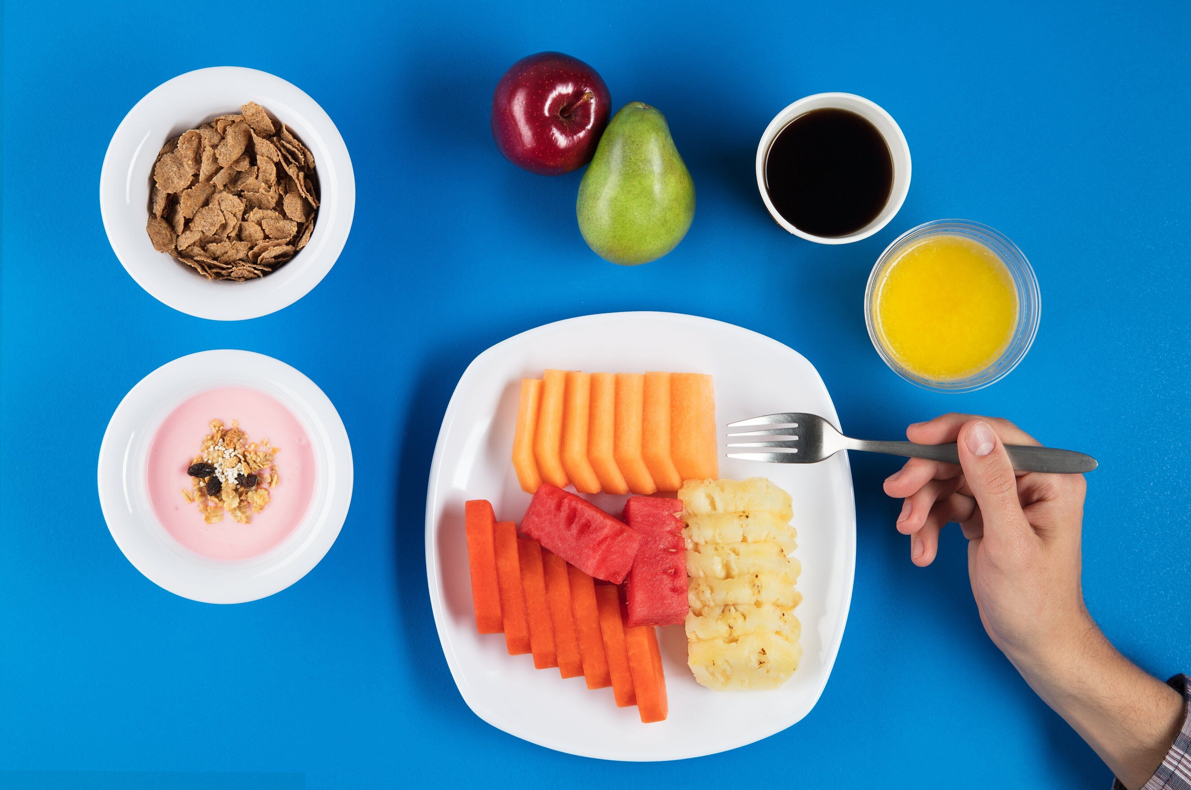 A meal with various fruits and vegetables on a plate, a bowl of cereal, and a cup of coffee on a blue background.