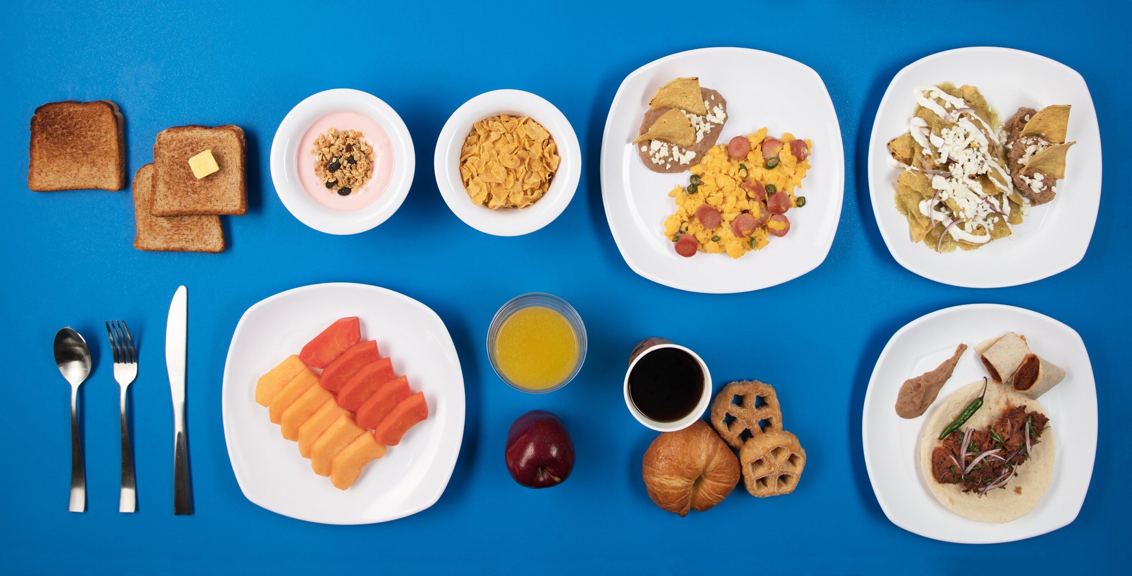 A breakfast spread with toast, yogurt, cereal, eggs, chilaquiles, and a croissant.