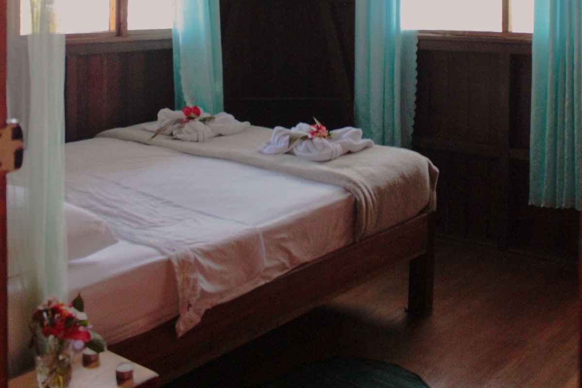 A wooden room with a bed, curtains, and a ceiling fan.