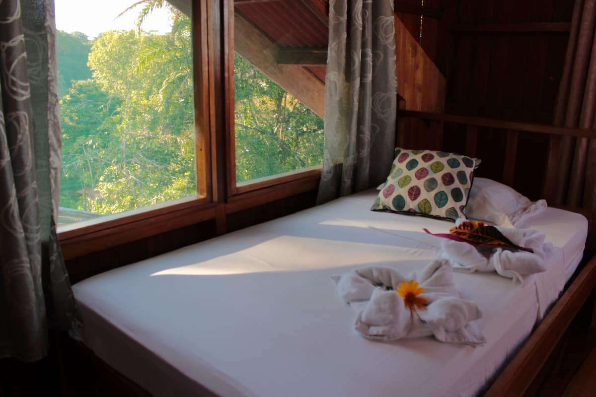 A bed with a pillow, a towel, and a flower.