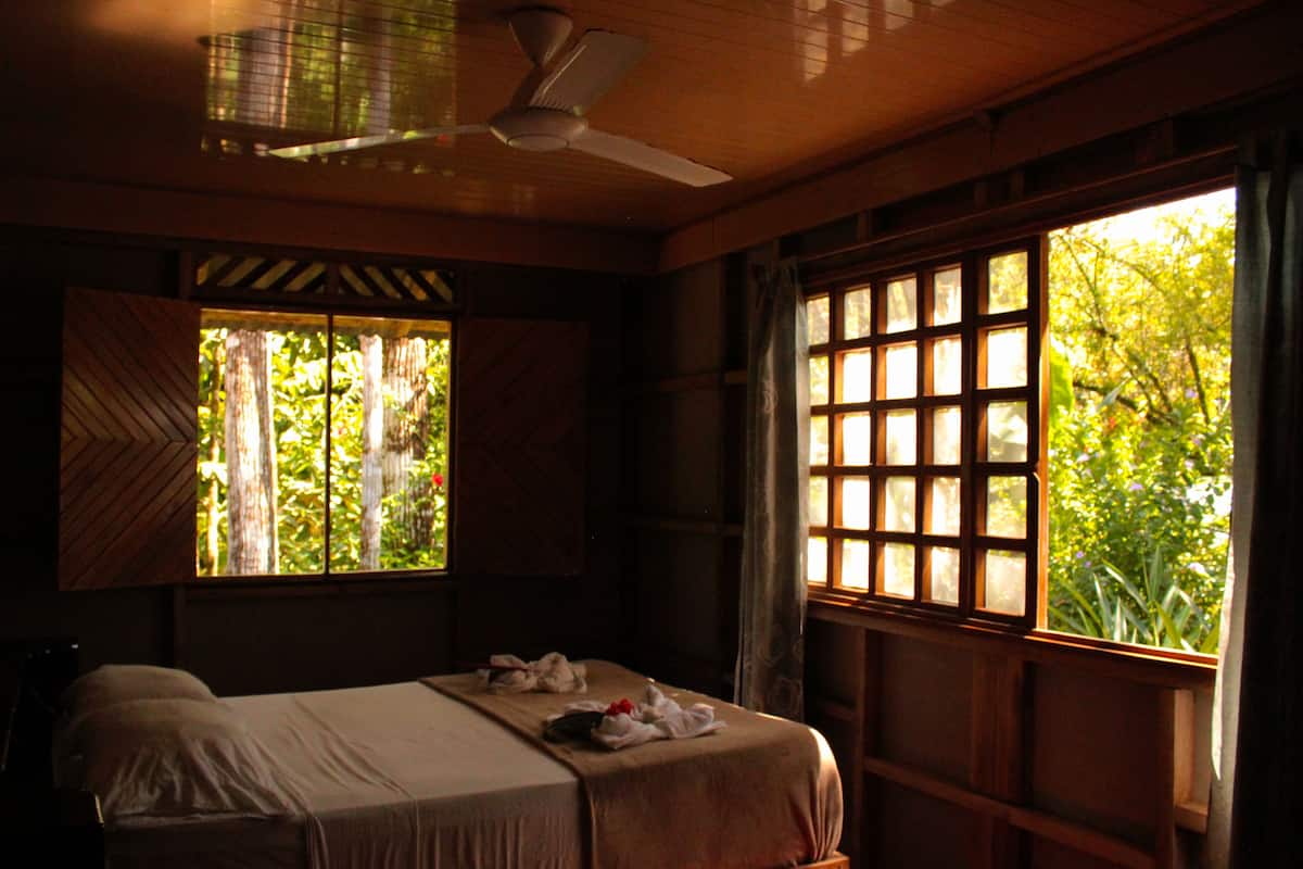 A bedroom with a bed, a ceiling fan, and a window with a view of greenery.