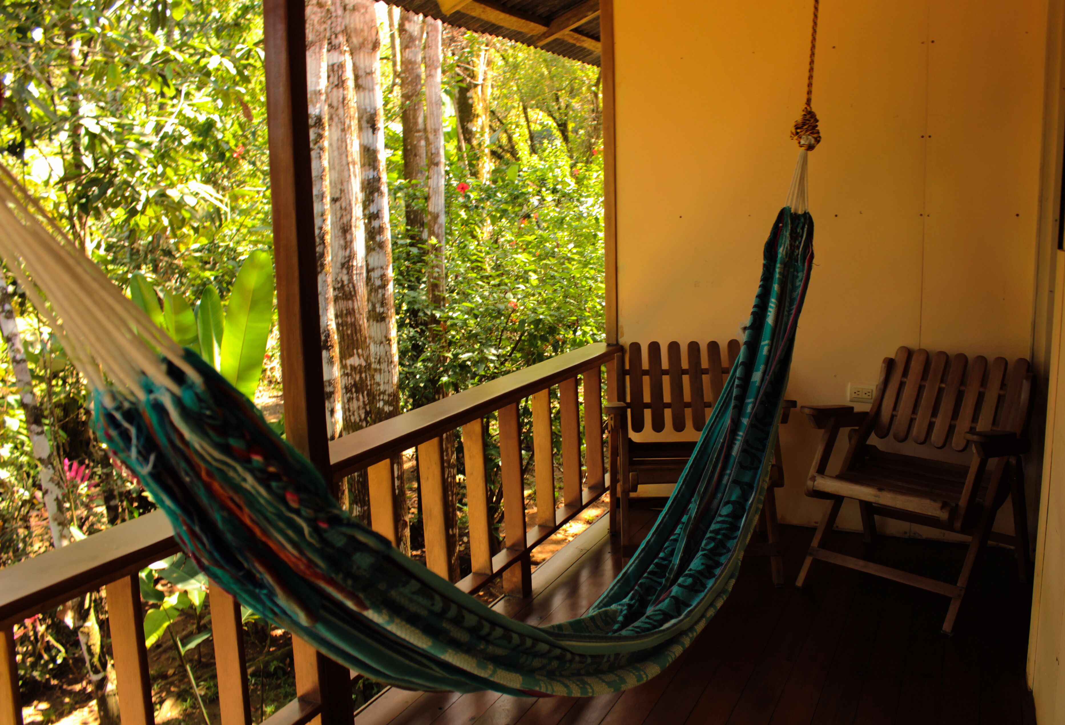 A hammock hanging on a wooden porch with a view of lush greenery.