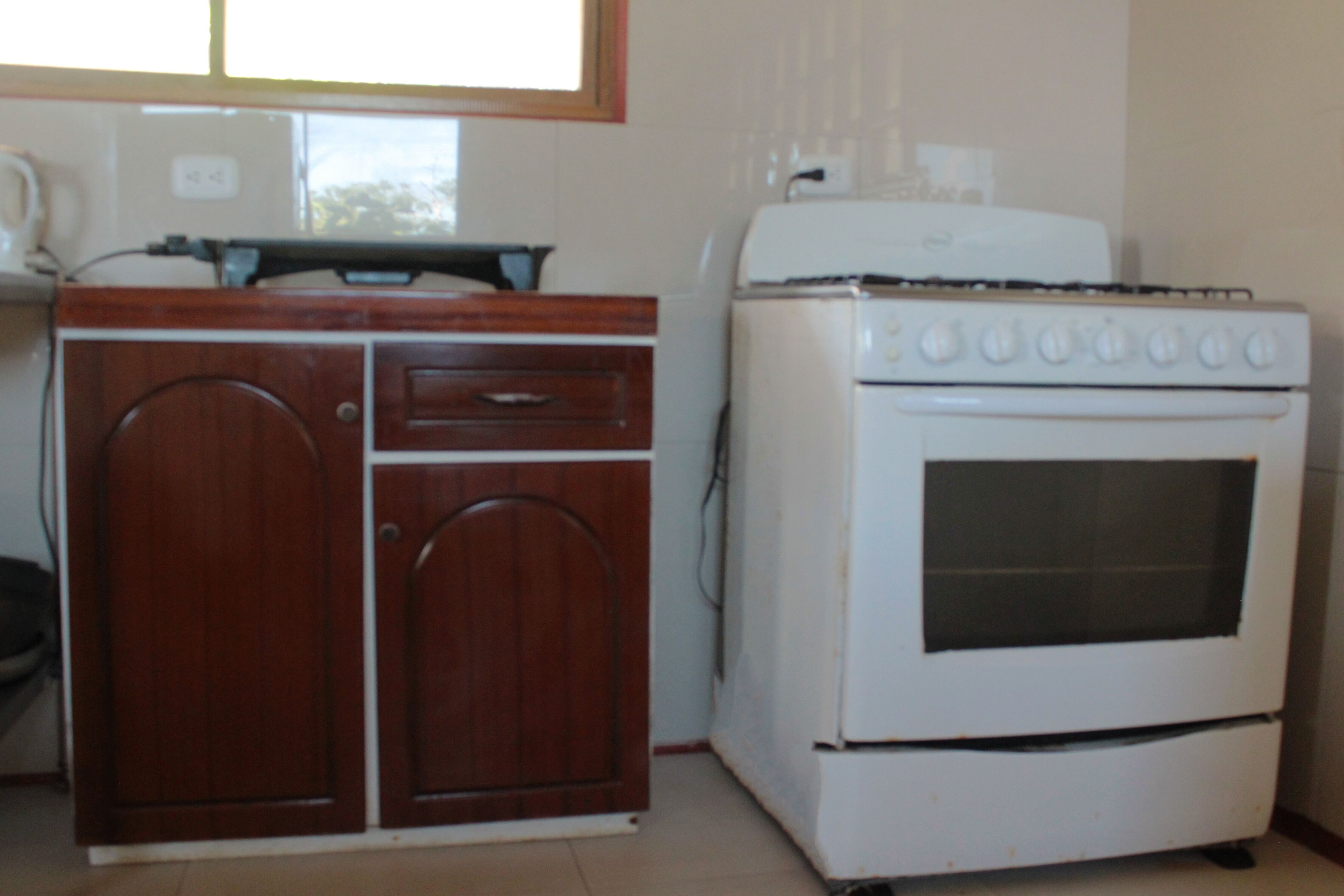 A kitchen with a stove, a wooden cabinet, and a window.
