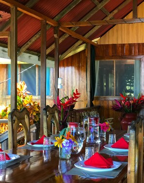 Une table à manger en bois, mise avec des serviettes rouges, de la verrerie transparente et des centres de table floraux.