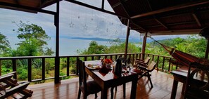 A wooden deck with a table set for two, overlooking a lush landscape with a view of mountains and a body of water. - Casa Horizontes Corcovado (Drake Bay)