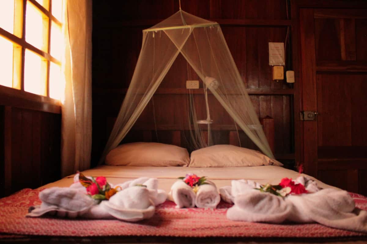 A bed with a mosquito net, two pillows, and towels with flowers on a patterned bedspread.