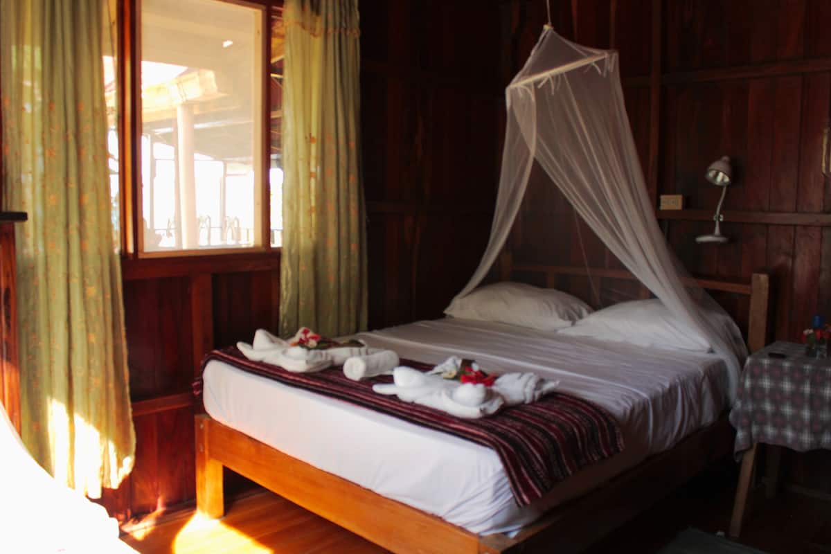 A wooden bed with a canopy, white linens, and towels arranged on the bed.