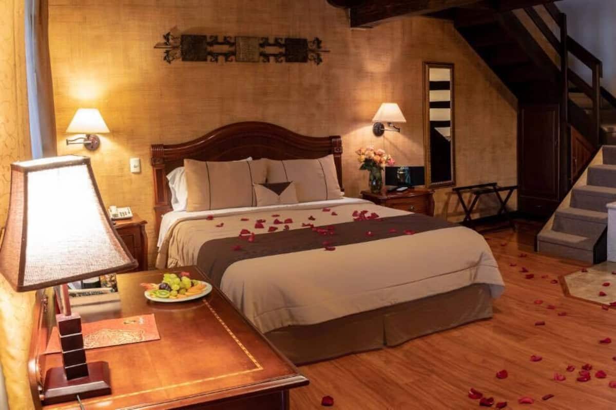 A cozy bedroom with a large bed, a wooden dresser, a desk, and a bathroom with a bathtub.