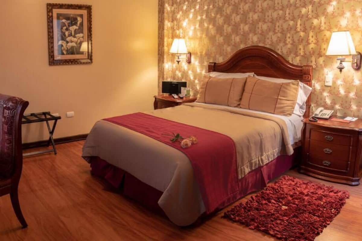 A hotel room with a wooden bed, a desk with a plate of fruit, a chair, and a red rug.