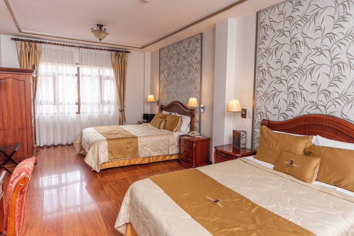A hotel room with two beds, wooden headboards, and a large floral wallpaper.