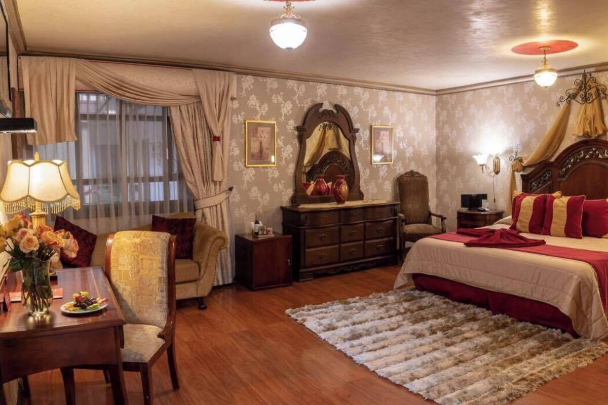 A hotel room with a bed, a desk with a lamp, a chair, a dresser, and a large mirror.