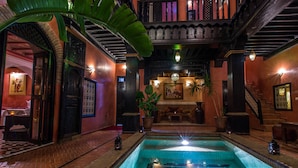 Una zona de piscina con suelo de baldosas, rodeada de muros con detalles decorativos y una escalera.