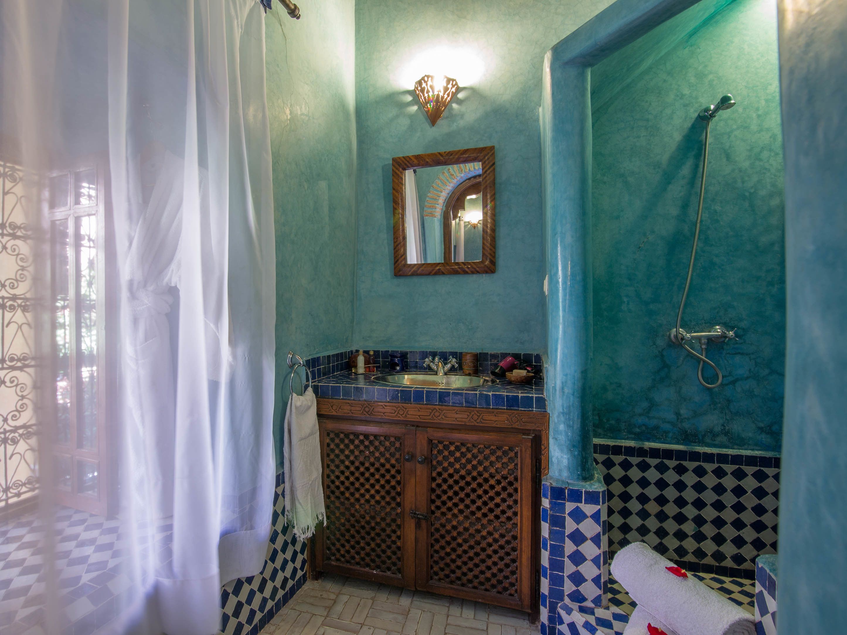 Un baño con pared de azulejos azules, un armario de madera, un espejo y una ducha.