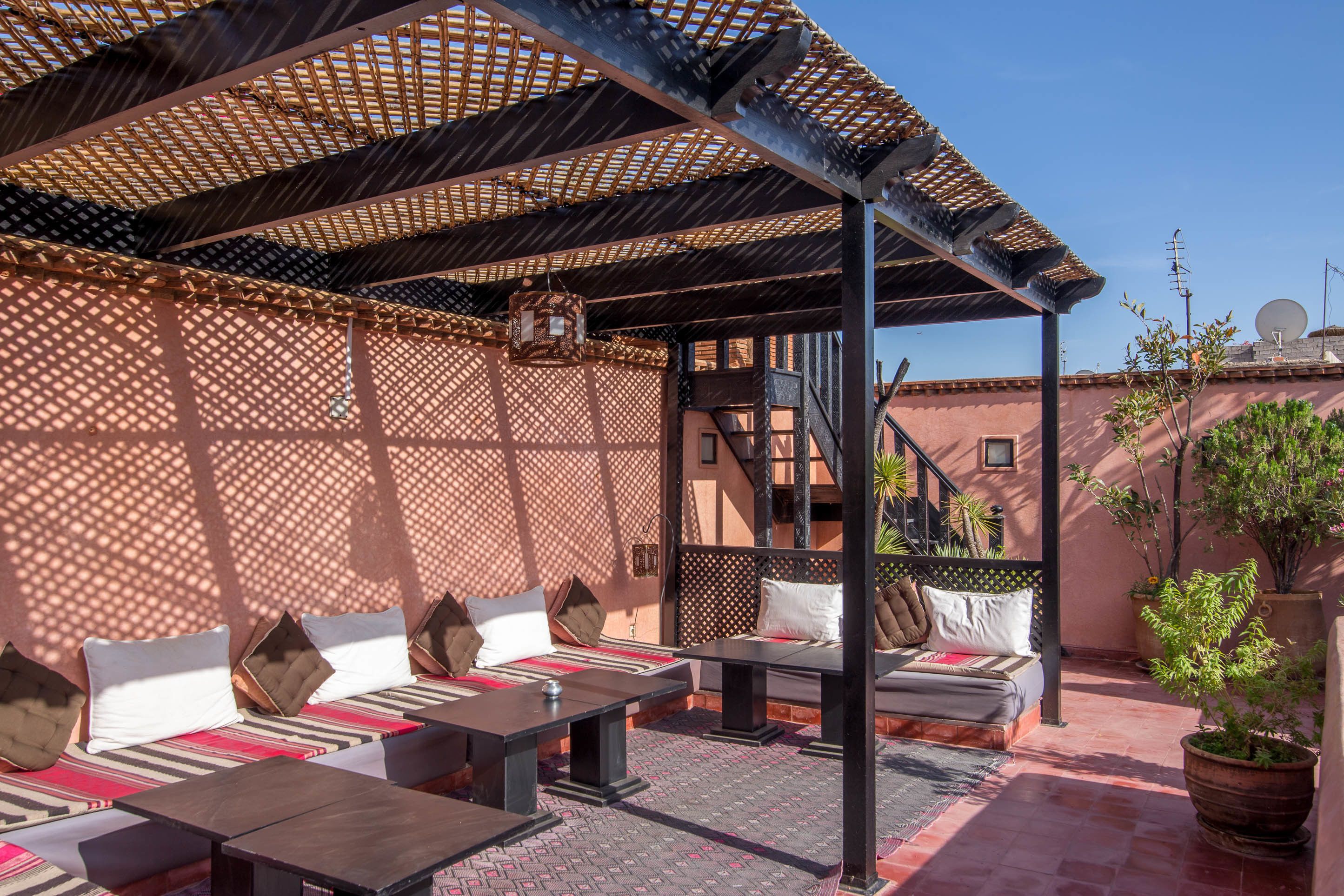 An outdoor seating area with multiple tables and benches, a pergola structure, and potted plants.