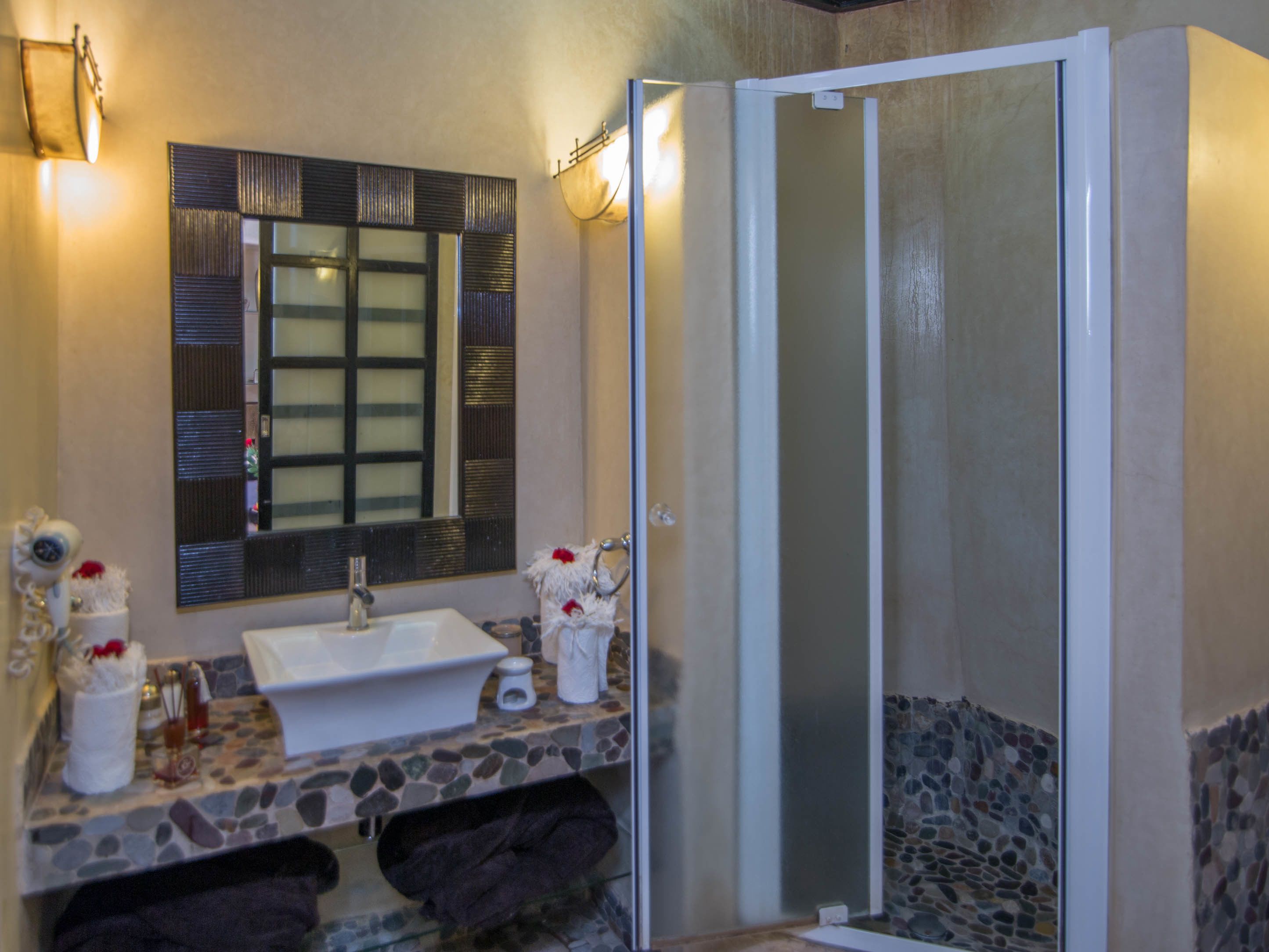A bathroom with a stone countertop, a white sink, a mirror, and a glass shower enclosure.