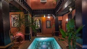 Zona de piscina con piso de baldosas, plantas en macetas y una escalera con barandales ornamentados.