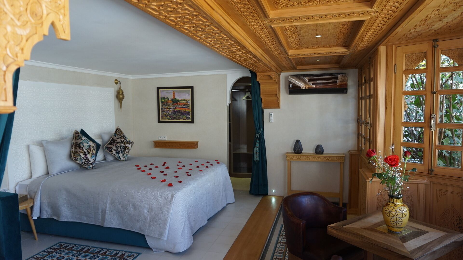 A bedroom with a bed, pillows, a bedside table, a chair, a wooden cabinet with glass doors, and a painting on the wall.