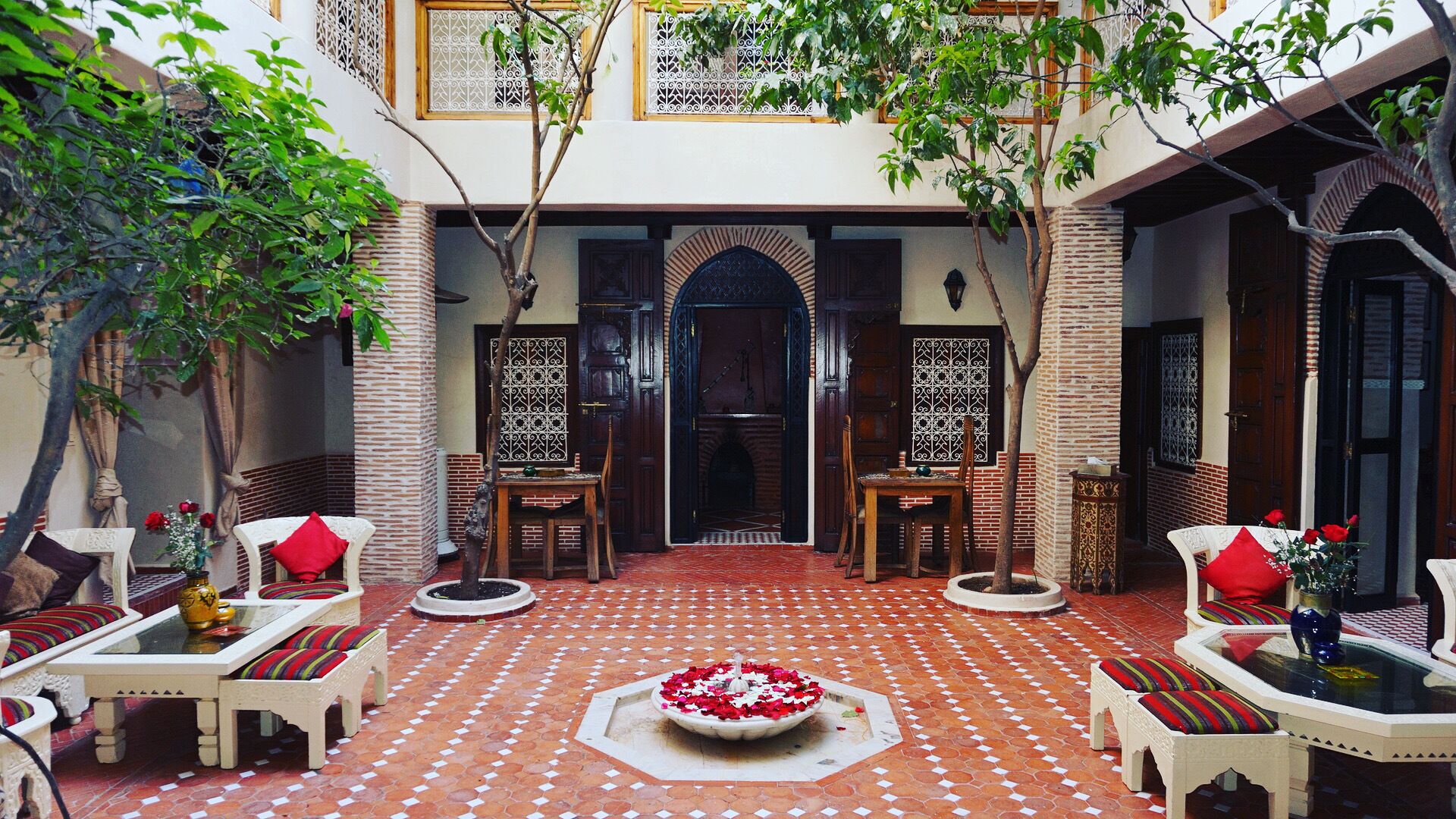 A courtyard with a tiled floor, two seating areas with chairs and tables, and a central decorative fountain.