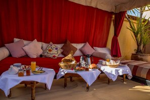 Una habitación acogedora con un fondo de cortina roja, un sofá con cojines y dos mesas con alimentos para el desayuno.