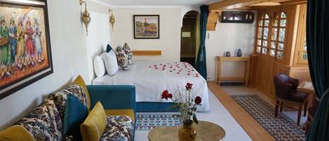 A hotel room with a bed, a sofa, a small table with a vase, and a view of the outside through a window.