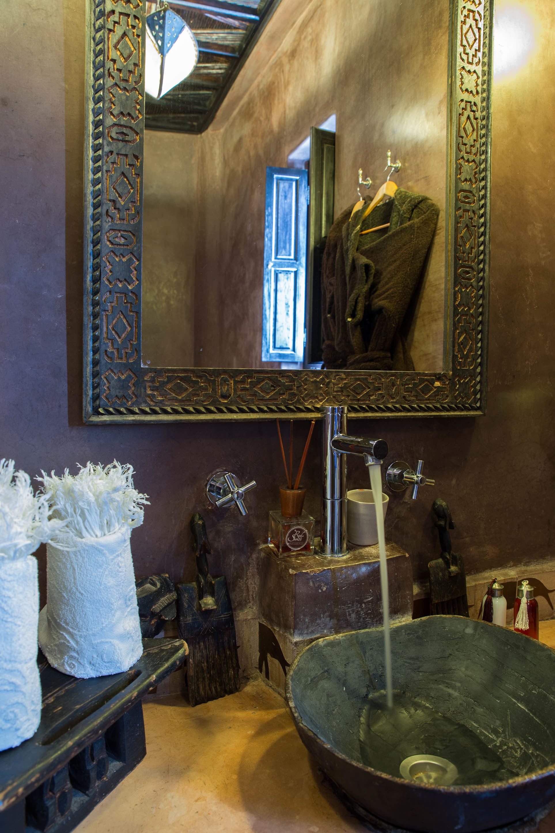 A bathroom with a large basin, a mirror with an ornate frame, and a towel rack with a towel.
