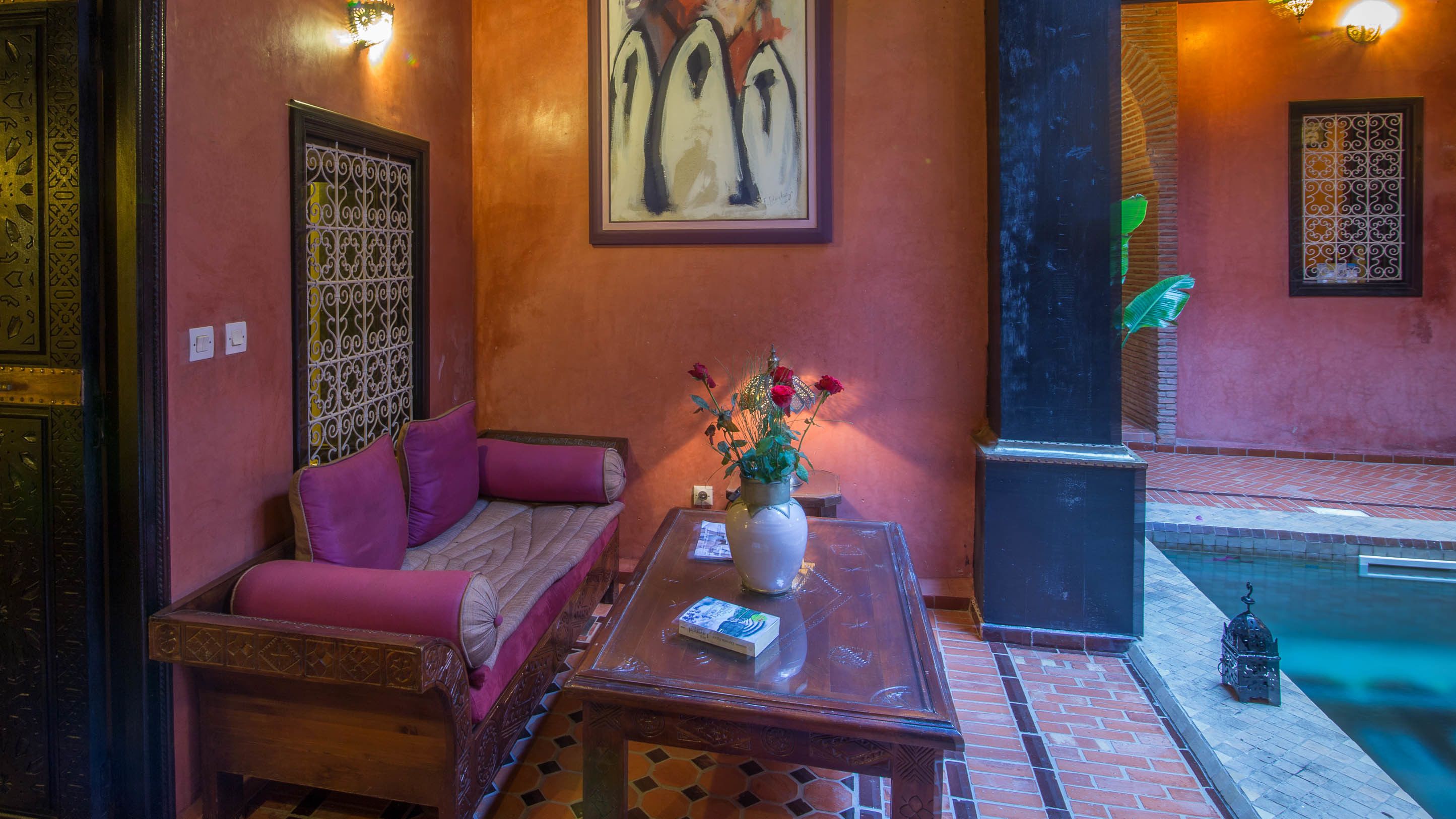 Un rincón acogedor con un sofá y una mesa, un jarrón decorativo con flores, y una piscina al fondo.
