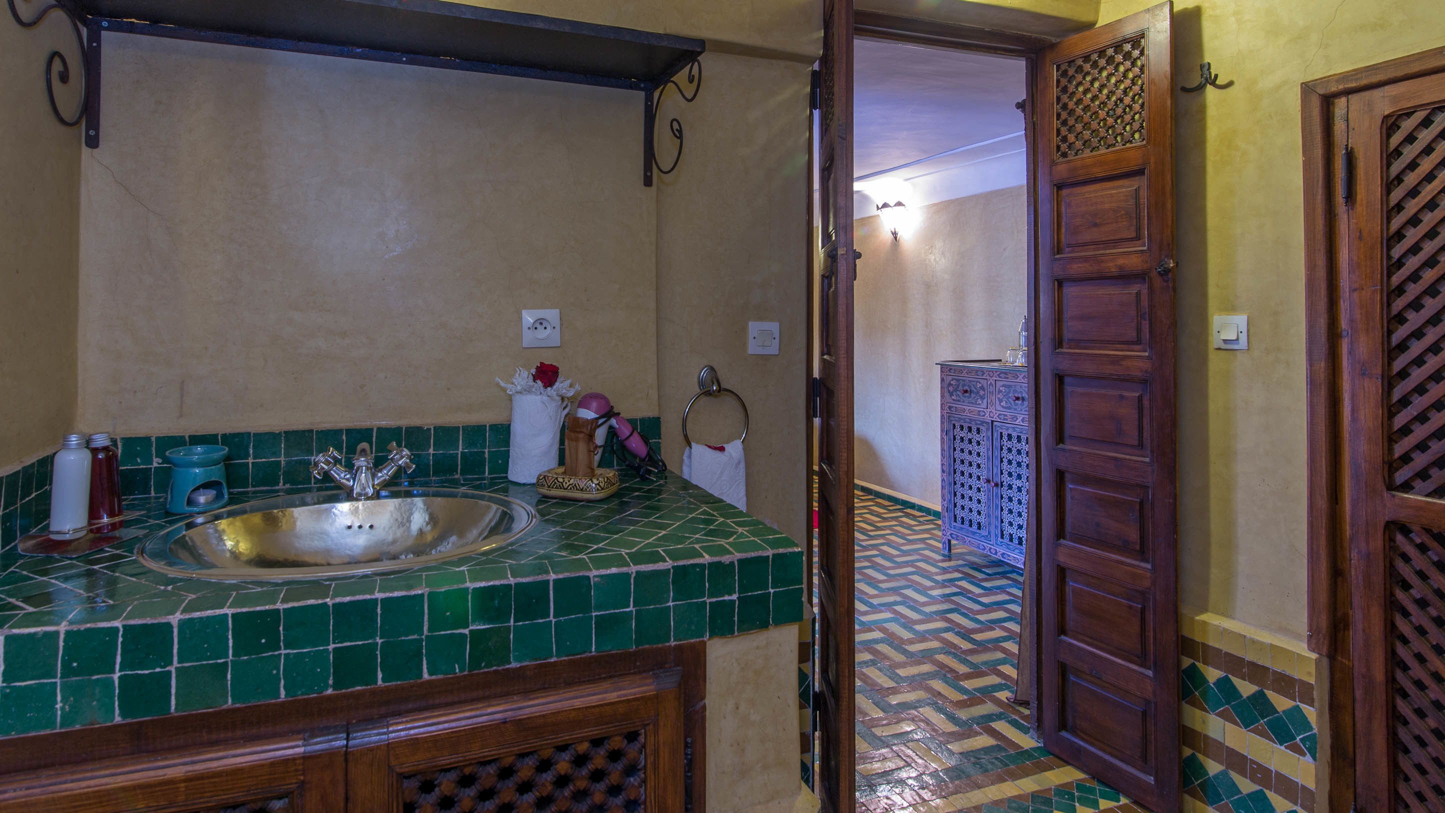 Un baño con un lavabo de azulejos verdes, un espejo y un armario de madera.