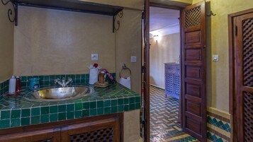 Un baño con un lavabo de azulejos verdes, un espejo y un armario de madera.