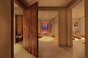Un couloir avec une cloison en bois, un espace détente avec des chaises longues et une vue sur une scène éclairée.