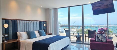 Een moderne hotelkamer met een groot bed, een televisie en een balkon met uitzicht op zee.