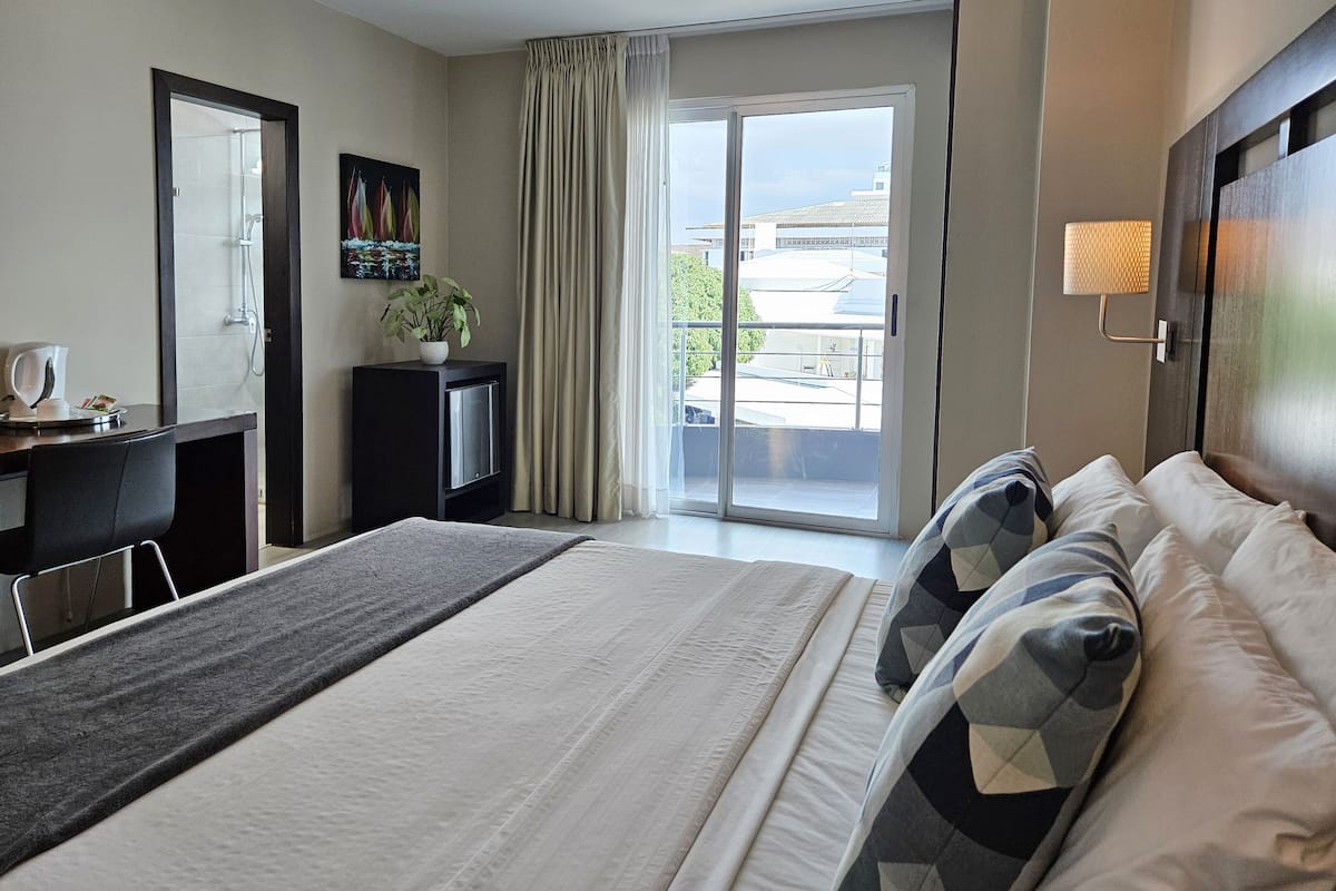 A hotel room with a bed, a desk, a television, a plant, and a view of the outside.