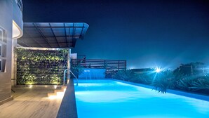 A swimming pool with a waterfall feature, surrounded by a wooden deck and a wall of greenery. - Hotel Perla Spondylus (Manta)