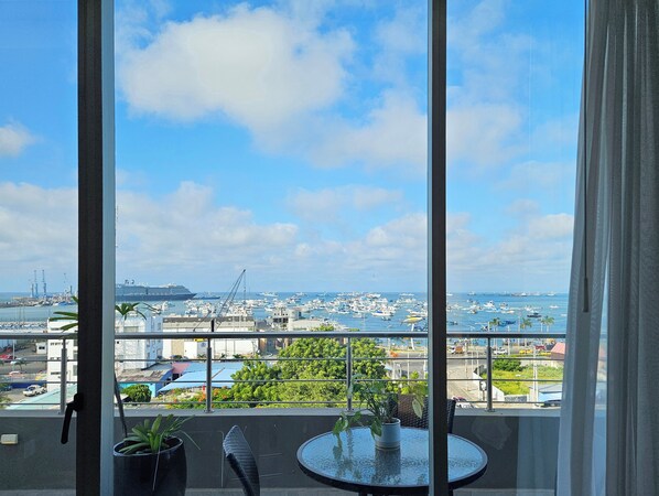 A balcony with a table and chairs, overlooking a marina with boats and a large cruise ship. - Hotel Perla Spondylus (Manta)