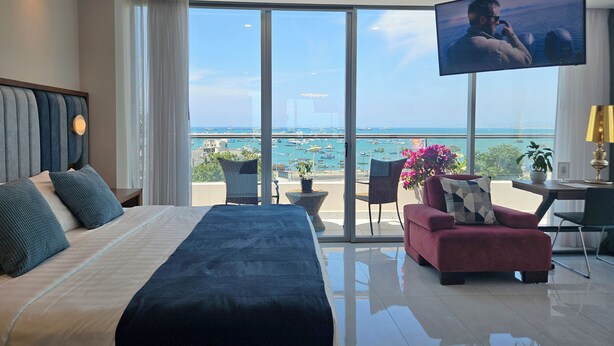 A modern hotel room with a large bed, a TV, a balcony with a view of the sea, and a dining area. - Hotel Perla Spondylus (Manta)