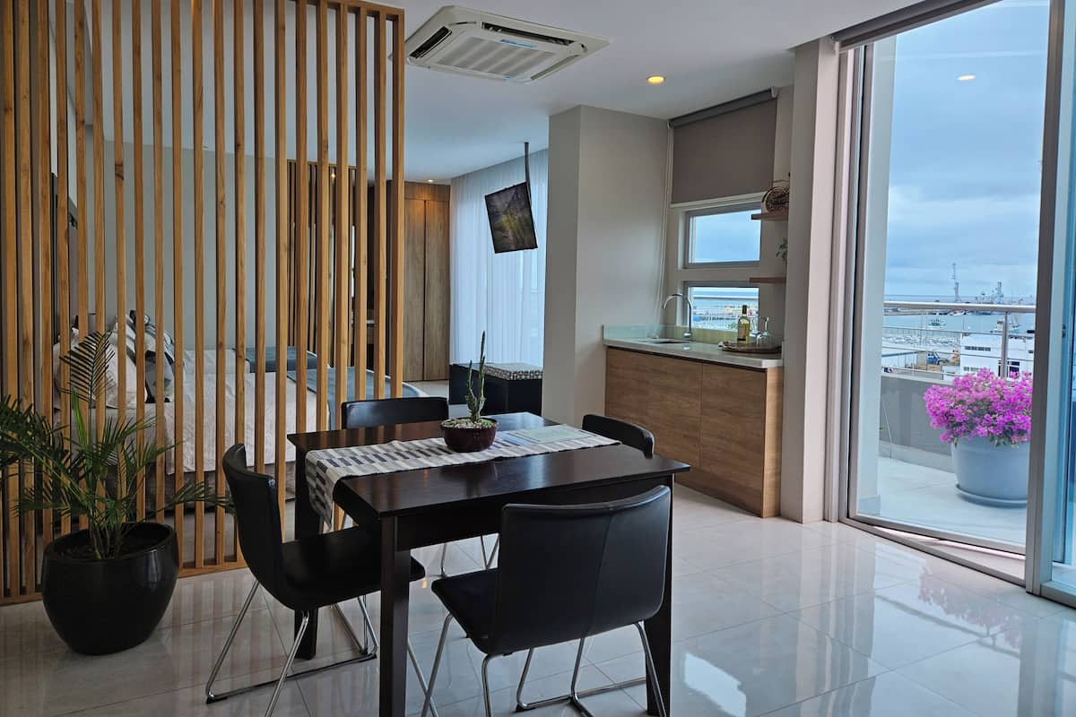 A modern dining area with a table, chairs, a potted plant, and a view of the city through large windows.